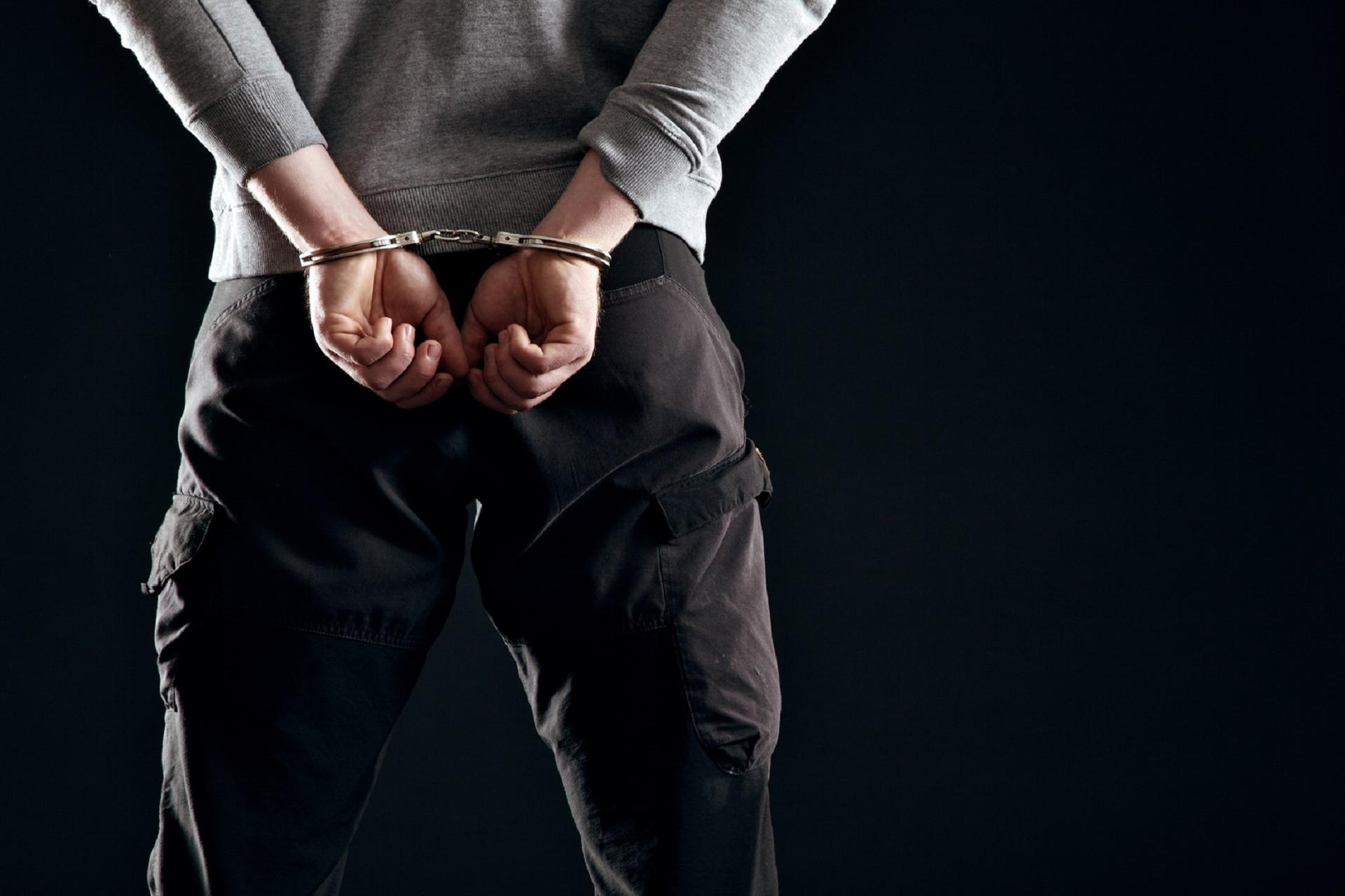 Murderer locked in handcuffs isolated on black